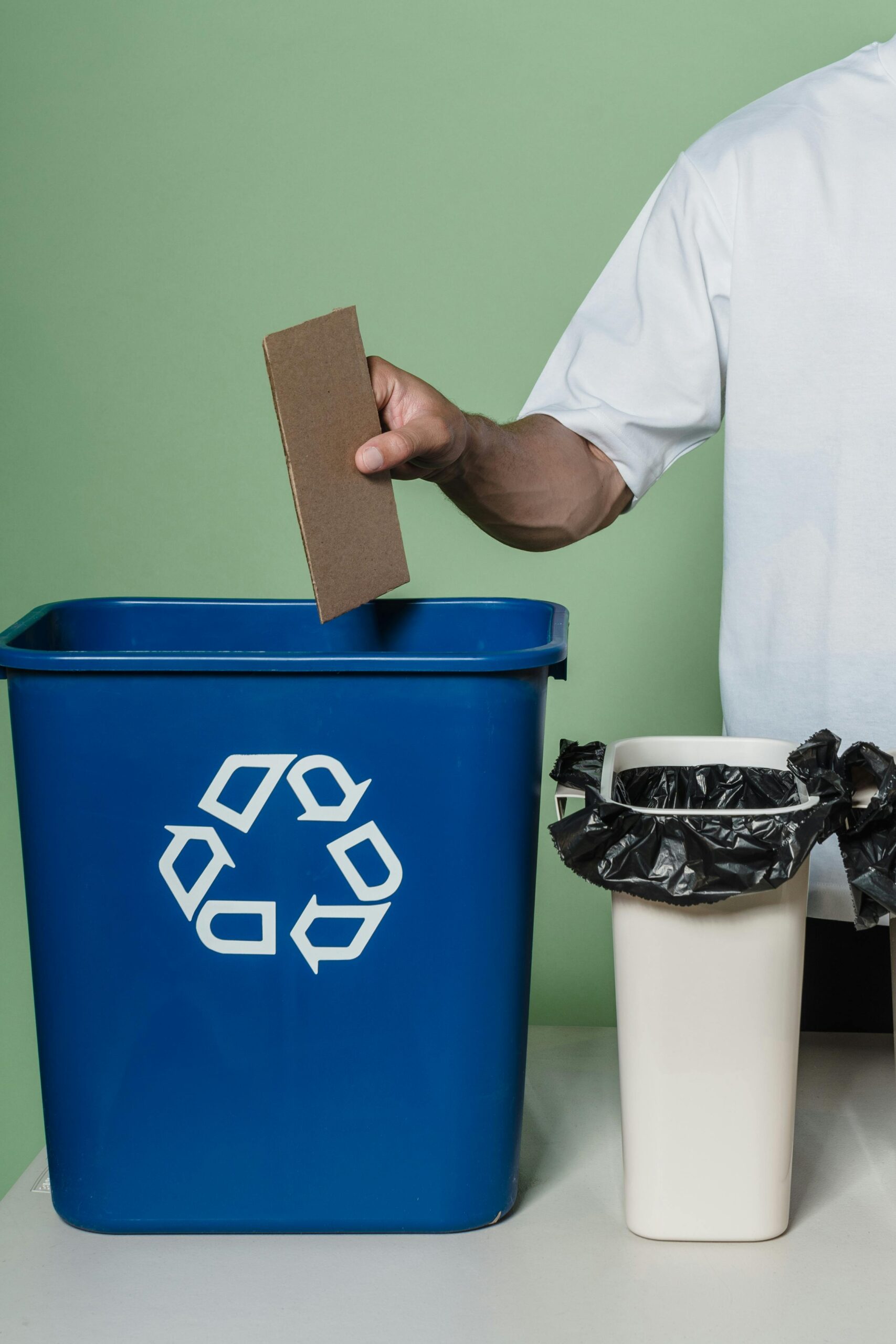 A person placing cardboard into a blue recycling bin, promoting eco-friendly practices indoors.